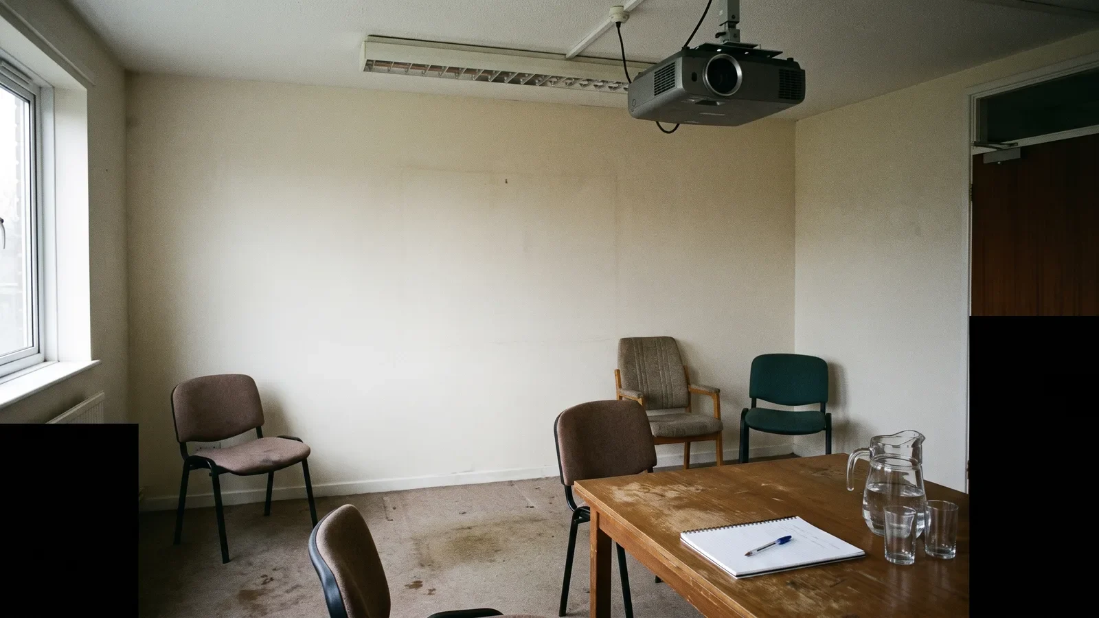 Small meeting room with ceiling projector, blank wall and notepad set up before a vendor demo